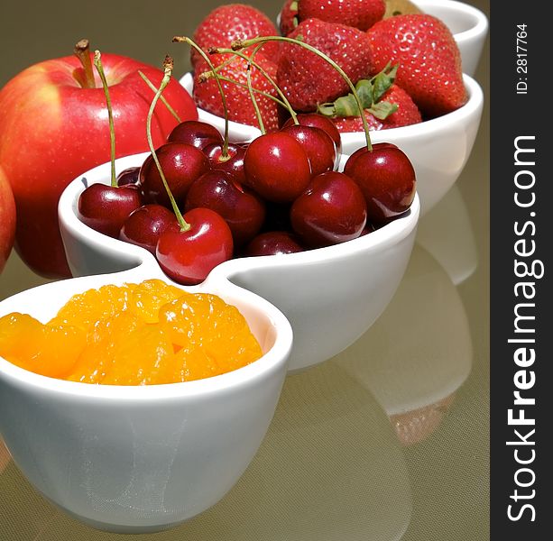 Small bowls of strawberries, cherries, and manderine orange slices with apples in the back. Small bowls of strawberries, cherries, and manderine orange slices with apples in the back.