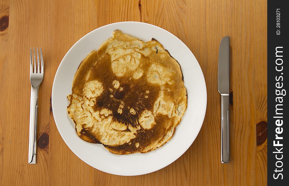 Top view on burnt pancake on white plate