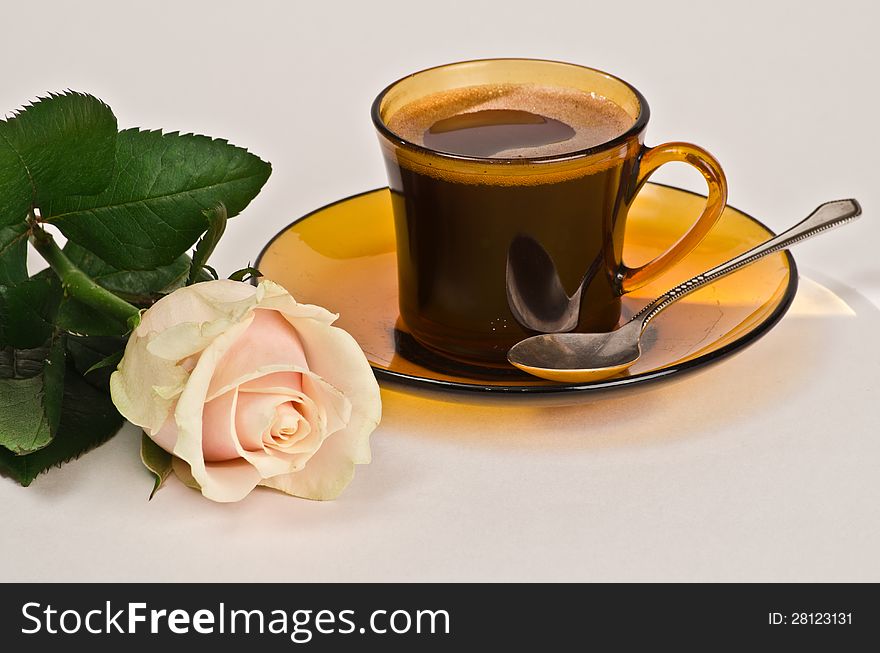 On a white background - yellow cup of coffee on a yellow saucer, near the beautiful rose bud. On a white background - yellow cup of coffee on a yellow saucer, near the beautiful rose bud.