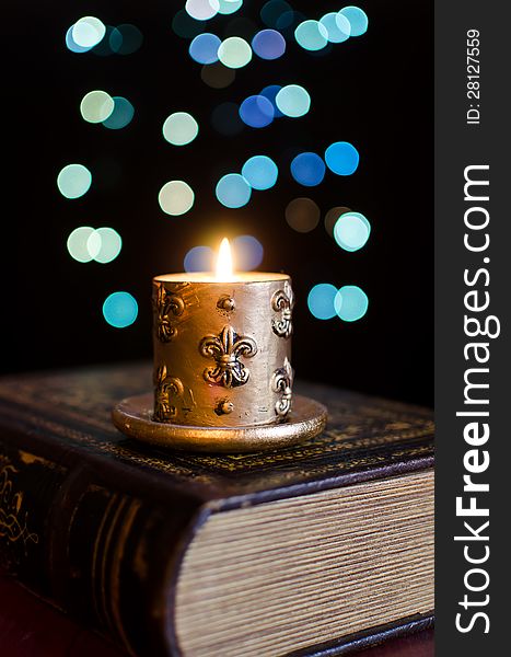 Burning candle and old book on bokeh background