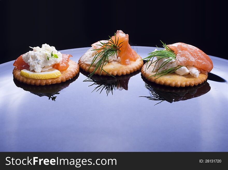 Light snack from smoked salmon with soft cheese and herbs on crackers.