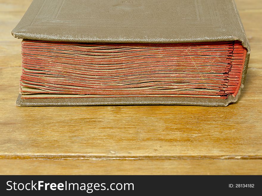 Fragment of old book laying on the weathered wooden surface with selective focus on red pages. Fragment of old book laying on the weathered wooden surface with selective focus on red pages