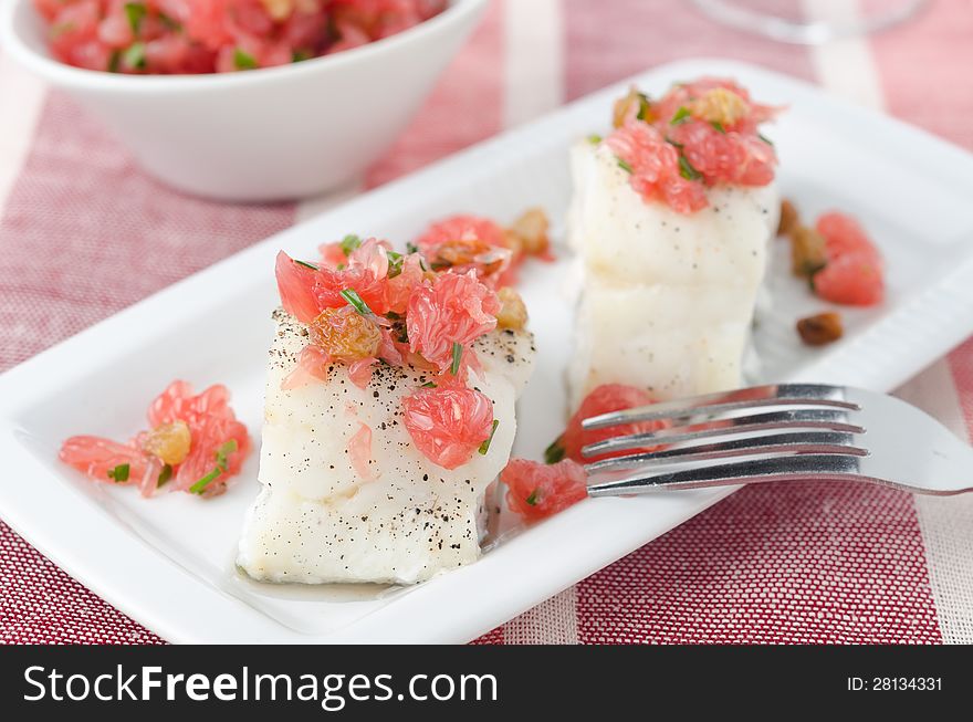 Baked cod with grapefruit salsa on white dish closeup