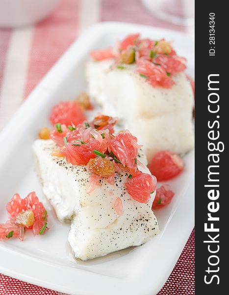 Baked cod with grapefruit salsa on white dish closeup. Baked cod with grapefruit salsa on white dish closeup