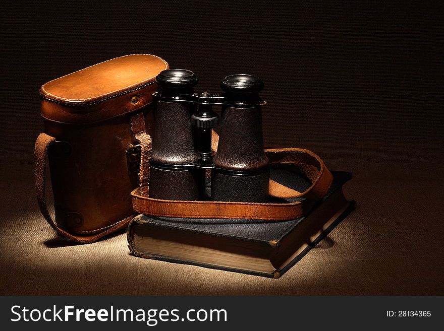 Still life with old binoculars on ancient book near leather case