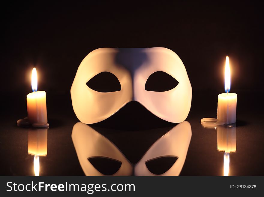 White mask between lighting candles on dark background. White mask between lighting candles on dark background
