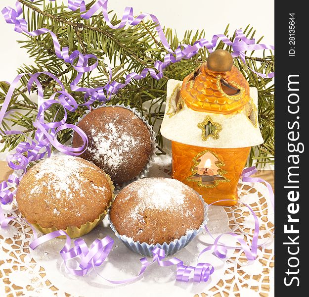 Three brown muffins with sugar powder, conifer and the yellow lantern. Three brown muffins with sugar powder, conifer and the yellow lantern