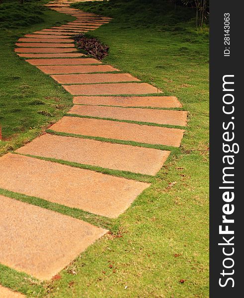 Walkway formed using granite stone slabs in a garden with lush green grass(lawn) on either side. The place is very tranquil and the walk way forms a S curve.