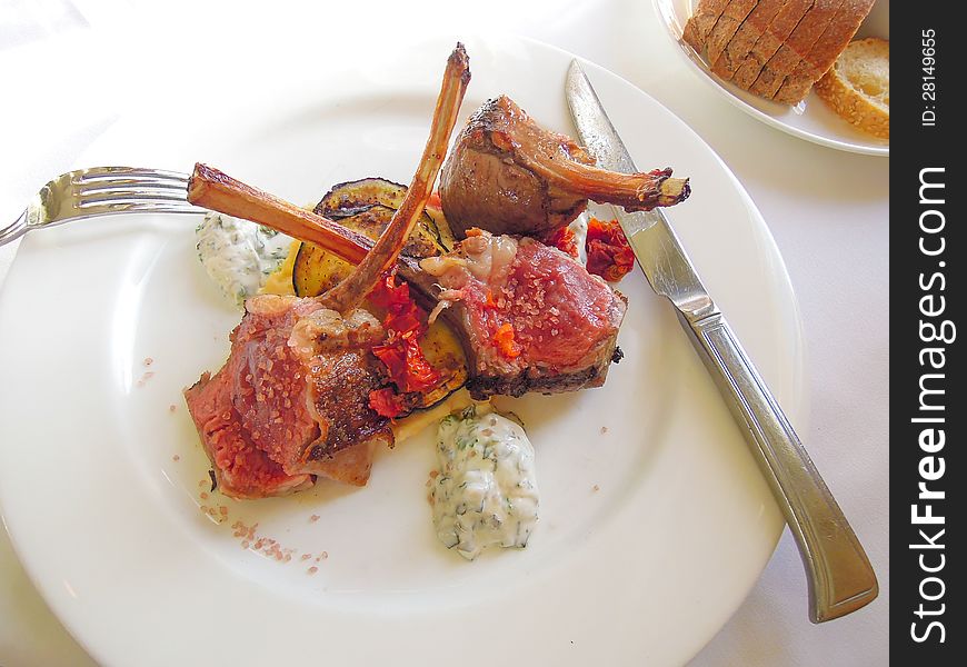 Lamb chops cooked very rare served on a bed of vegetables on a white plate. Lamb chops cooked very rare served on a bed of vegetables on a white plate.