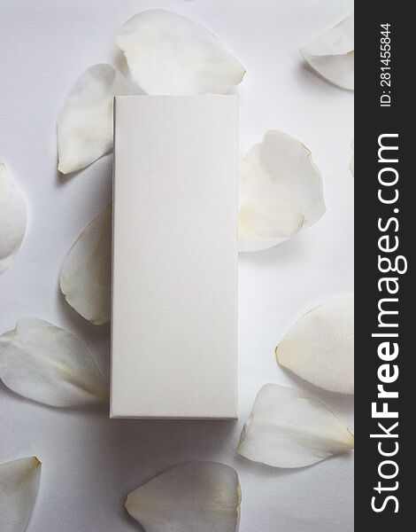 Product photo of a white box of natural cosmetics, on a white background and camellia petals, vertical photo, product photo, for mockups