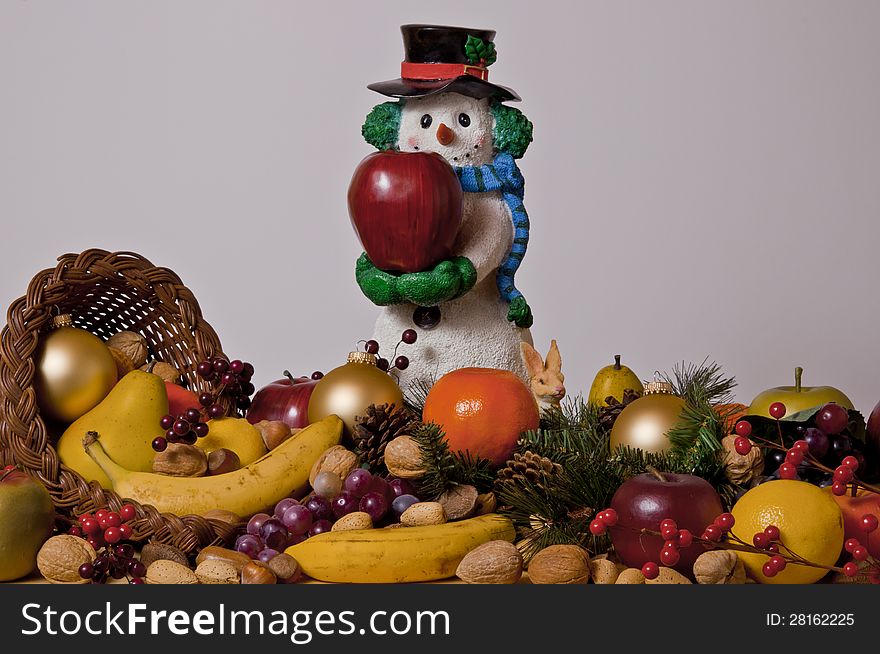 Snowman figurine holding apple surrounded by a cornucopia of fruits and nuts