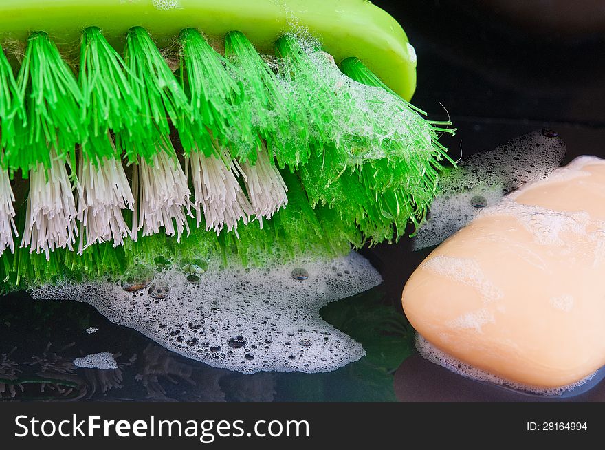 Brush for washing hands and a piece of green soap with foam shot against a black background. Brush for washing hands and a piece of green soap with foam shot against a black background
