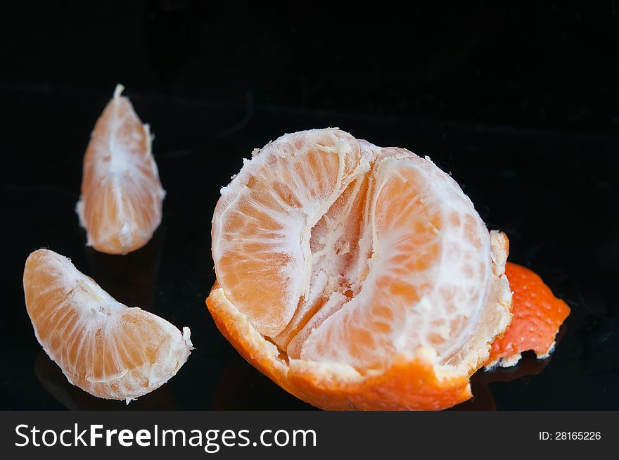Half of tangerine with peel and two slices photographed against a black background. Half of tangerine with peel and two slices photographed against a black background