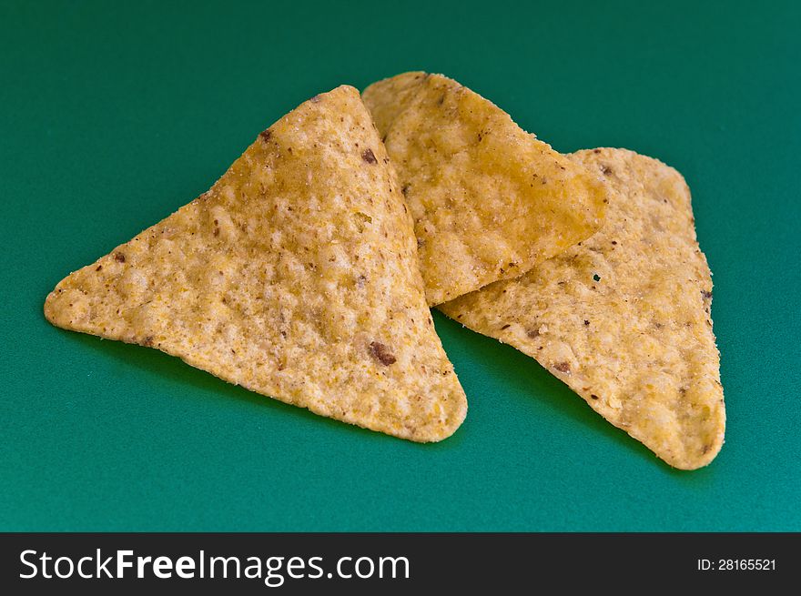 Three corn chips against green background are photographed close-up