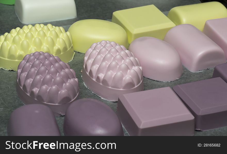 Rows of colorful homemade bath soaps drying on wax paper. Depth of field focused on molded images in the middle row.