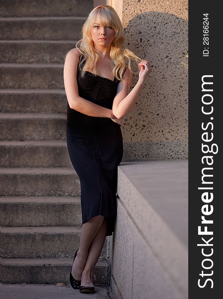 An image of a young woman in a black dress, standing in front of an outdoor staircase at golden hour. An image of a young woman in a black dress, standing in front of an outdoor staircase at golden hour