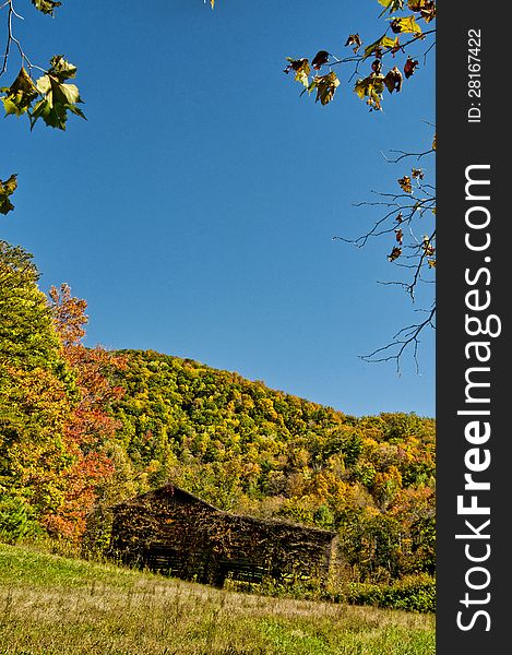 An Old Barn Sits Among Fall Leaves And A Blue Sky.