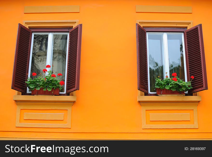 Orange wall with two traditional windows with wooden blinds and flowers on the sill. Orange wall with two traditional windows with wooden blinds and flowers on the sill.