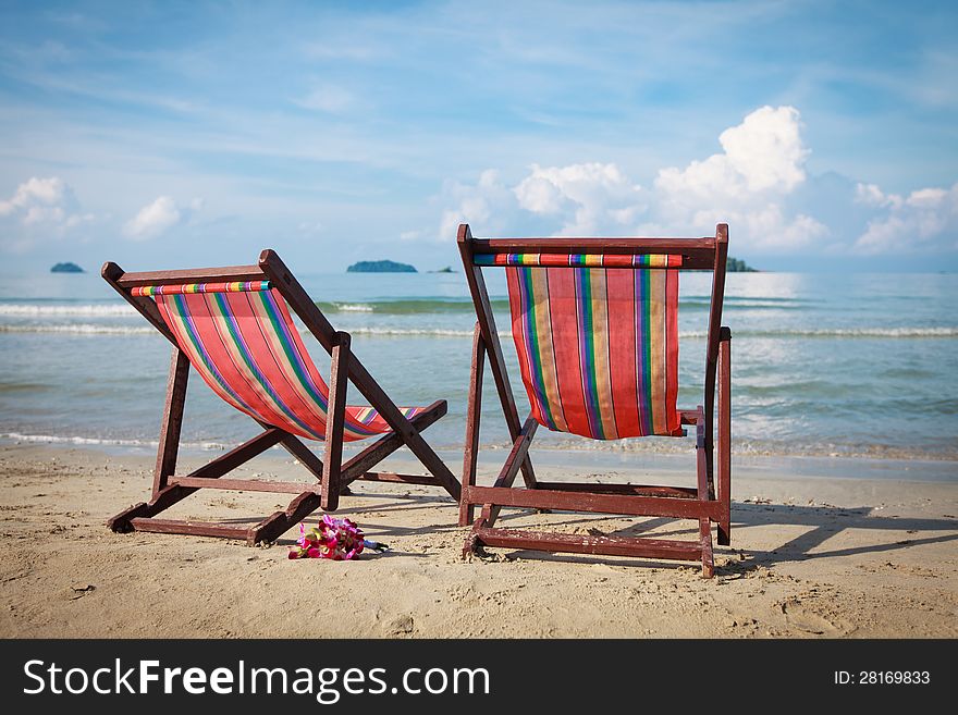 Two bright sun loungers on the beach. Bouquet of orchids in the sand.