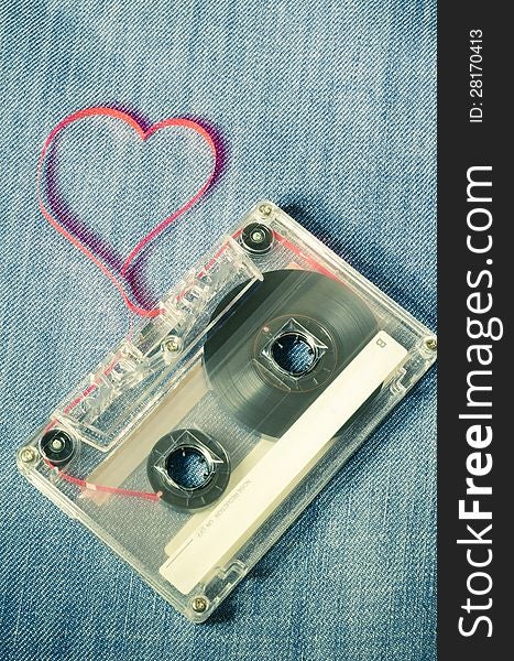 Vintage audio cassette on blue jeans with red tape pulled out as heart shape. Vintage audio cassette on blue jeans with red tape pulled out as heart shape