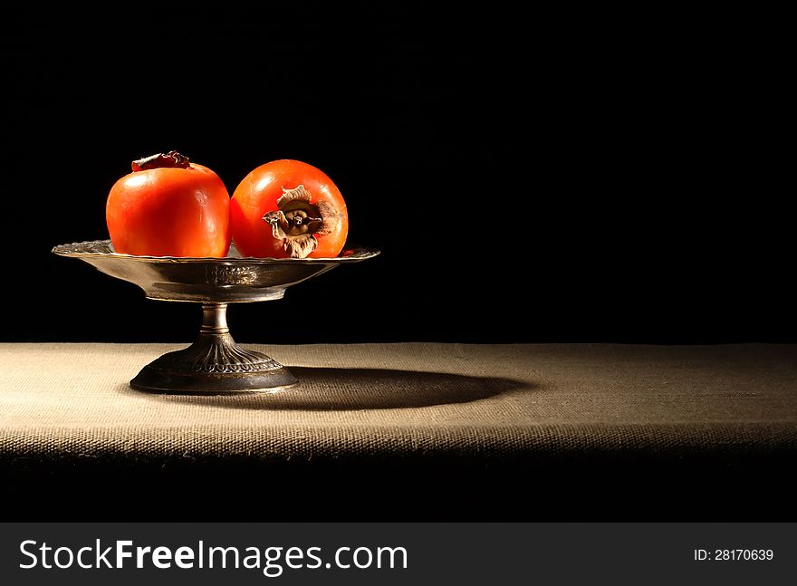 Vintage brass bowl with persimmon fruits on canvas surface. Vintage brass bowl with persimmon fruits on canvas surface