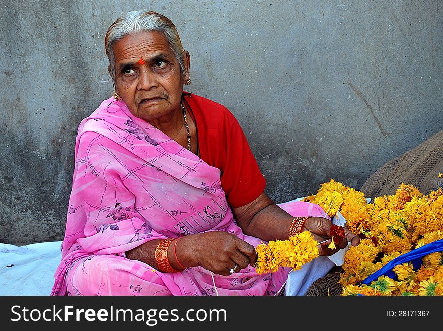 A flower seller making garland for the temple deities. A flower seller making garland for the temple deities