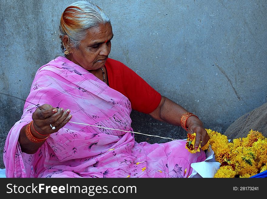 A flower seller making garland for the temple deities. A flower seller making garland for the temple deities