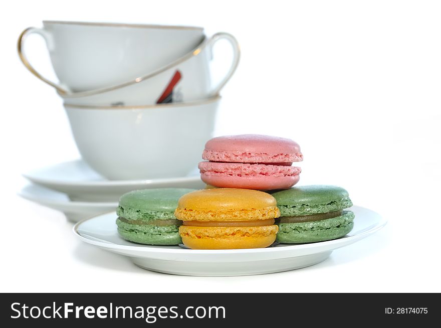 Porcelain coffee cups piled behind a plate of macaroons different colors. Porcelain coffee cups piled behind a plate of macaroons different colors