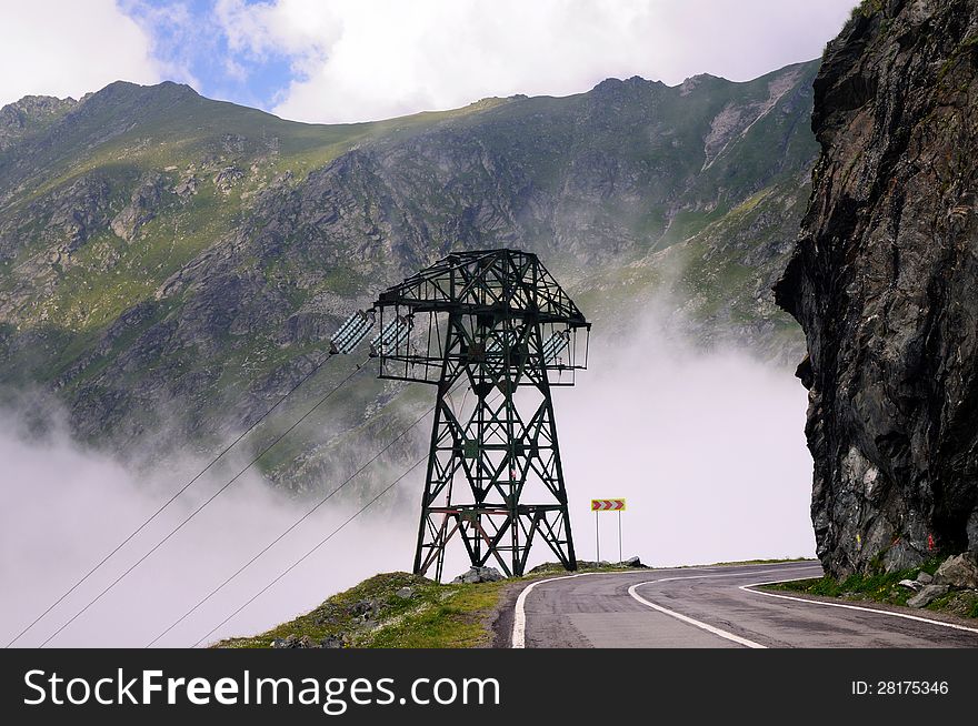 View of a foggy mountain road with electric pole on its left.