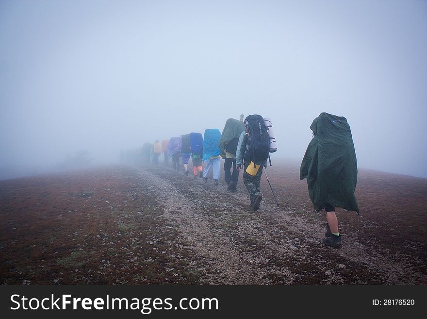 Group Of Tourists In Raincoats Disappearing Into Haze