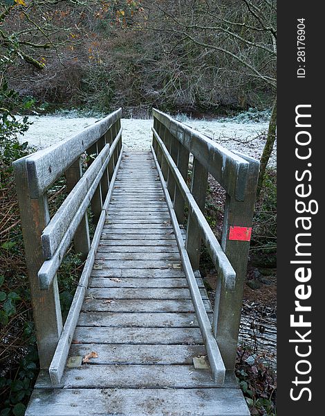 Wooden footbridge crossing a river with frost covering the rails and the grass in the field beyond. Wooden footbridge crossing a river with frost covering the rails and the grass in the field beyond.