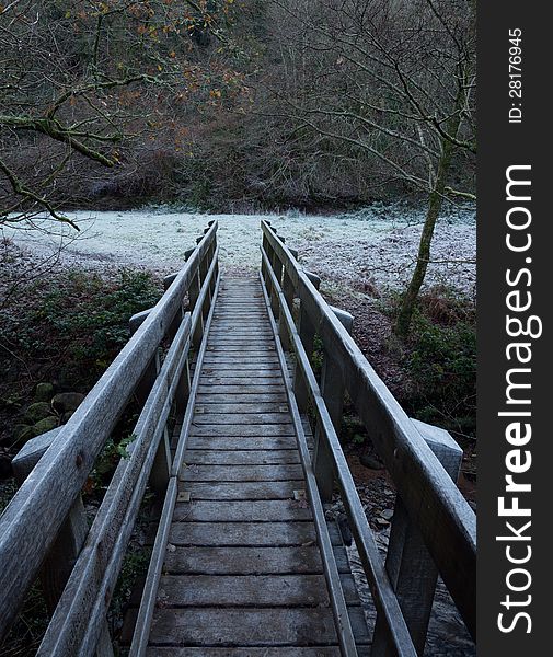 Wooden footbridge crossing a river with frost covering the rails and the grass in the field beyond. Wooden footbridge crossing a river with frost covering the rails and the grass in the field beyond.