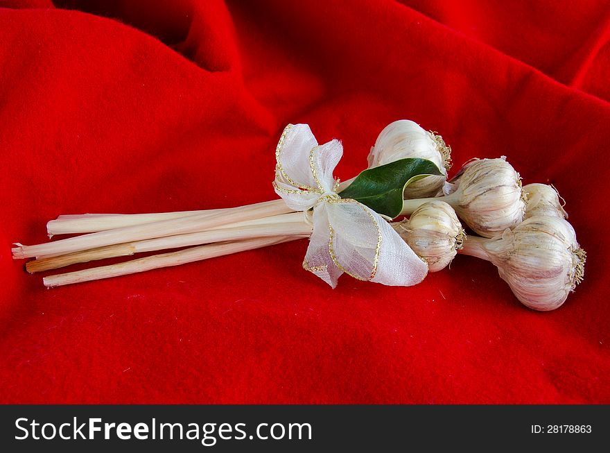 Bouquet of garlic bulbs tied with a white and gold ribbon for a Christmas gift on a background of red fabric.