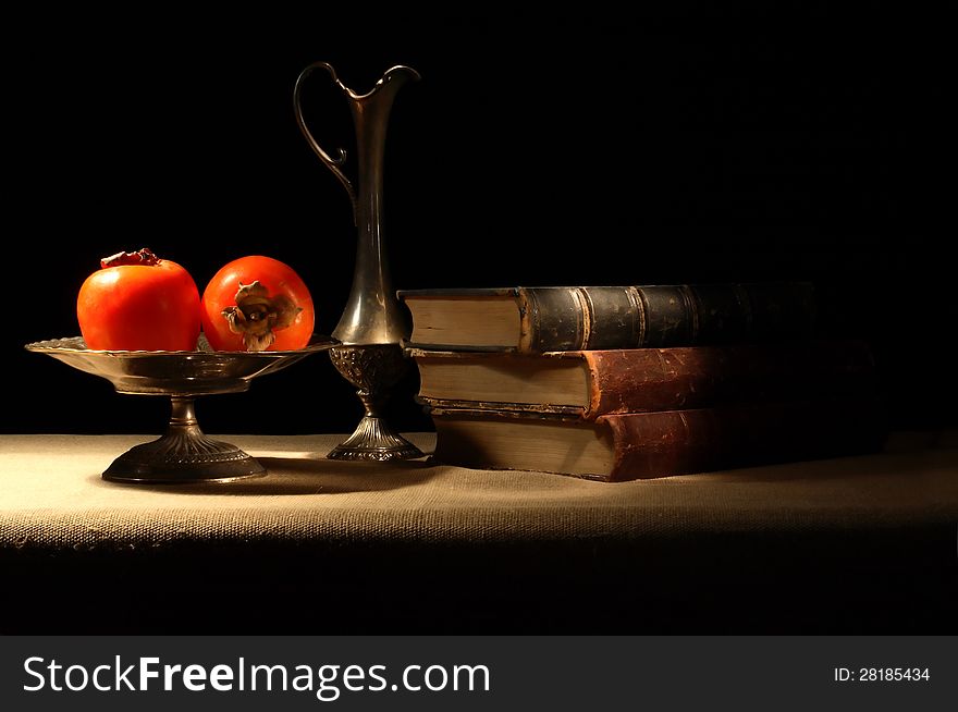 Vintage still life with persimmons in bowl near old book on canvas surface. Vintage still life with persimmons in bowl near old book on canvas surface