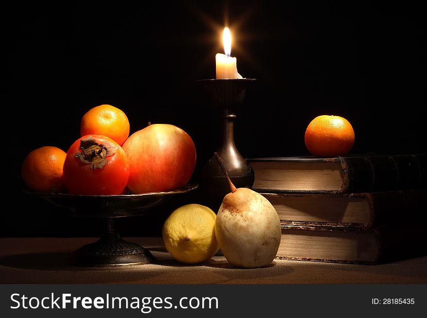 Vintage still life with fruits in bowl near old books and lighting candle. Vintage still life with fruits in bowl near old books and lighting candle