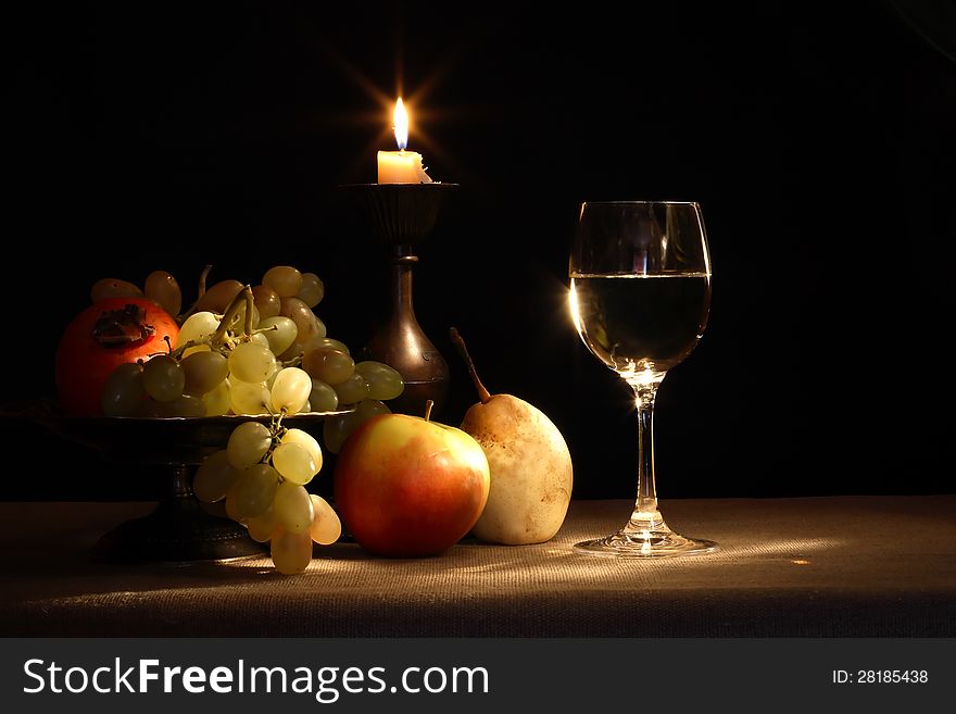 Vintage still life with fruits in bowl and wineglass near lighting candle. Vintage still life with fruits in bowl and wineglass near lighting candle