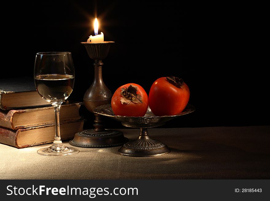 Vintage still life with fruits in bowl and wineglass near lighting candle and books