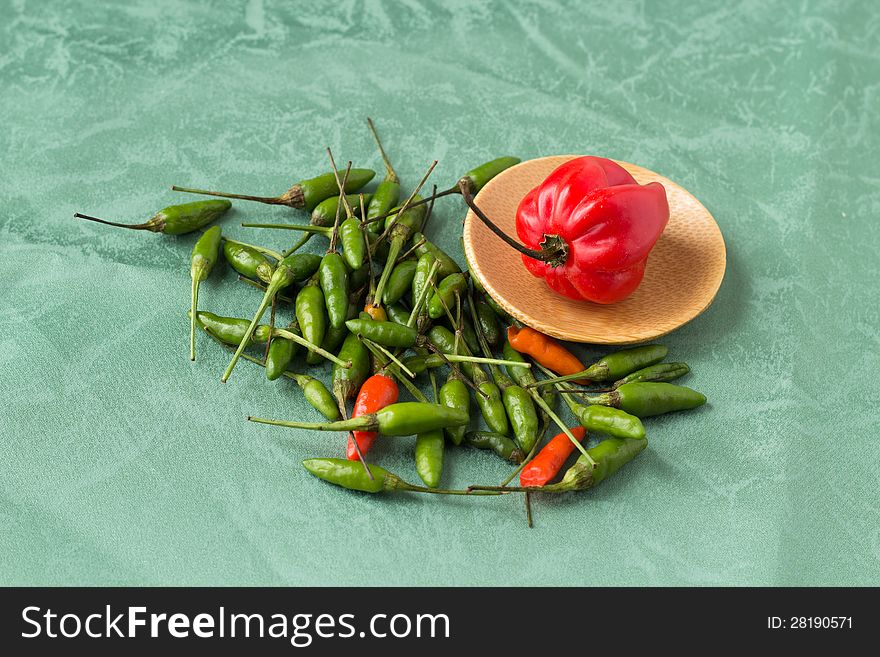 Red perrer in a wood plate with small green peppers around it. Green abstract background. Red perrer in a wood plate with small green peppers around it. Green abstract background.