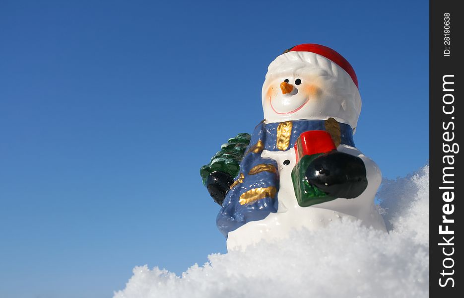 Smiling snowman figurine in snow with blue background