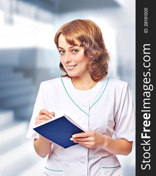 Young woman doctor in a white coat stands in hospital lobby. Young woman doctor in a white coat stands in hospital lobby