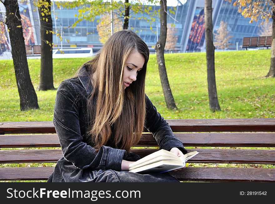 A girl in a park reads a book, sitting on a bench. A girl in a park reads a book, sitting on a bench