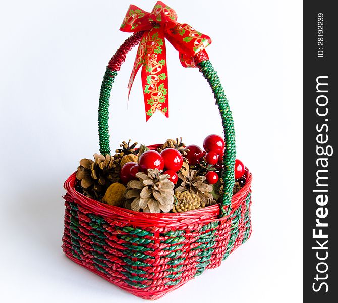 Decorative green and red wicker Christmas basket with a colorful ribbon on its handle and containing pine cones, nuts and cherries.