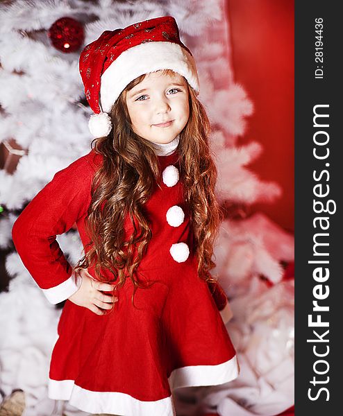 A little girl dressed as Santa Claus under the Christmas tree