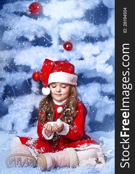 A little girl dressed as Santa Claus under the Christmas tree