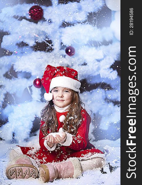 A little girl dressed as Santa Claus under the Christmas tree