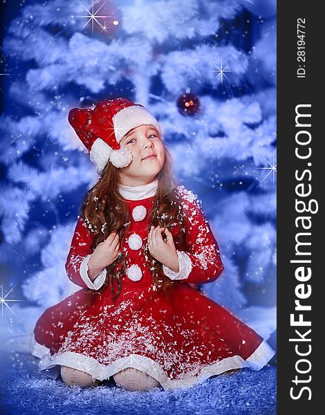 A little girl dressed as Santa Claus under the Christmas tree