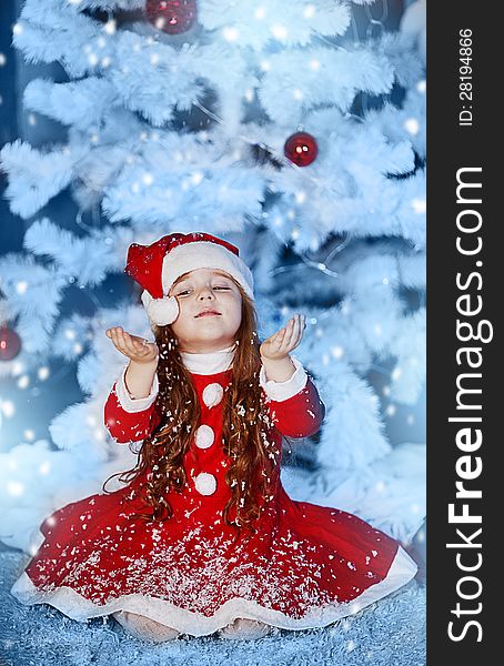 A little girl dressed as Santa Claus under the Christmas tree