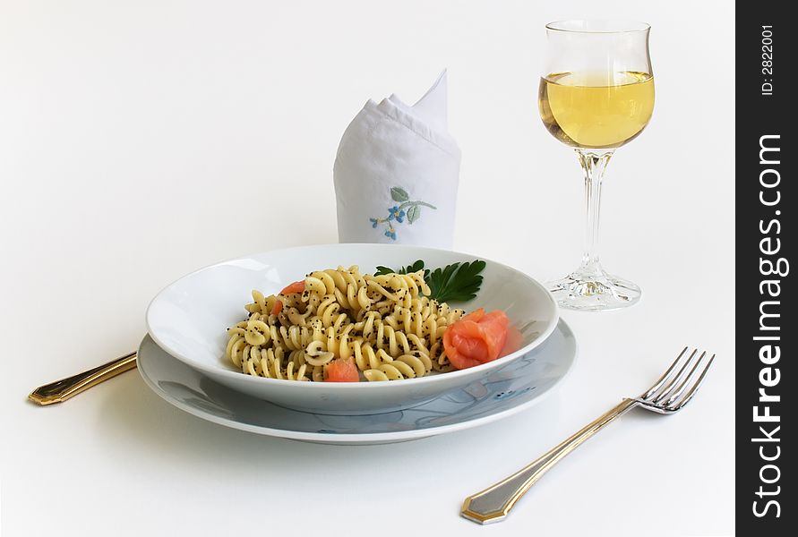 Prepared table with place settings, a glass of white wine, a dish with pasta and salmon. Prepared table with place settings, a glass of white wine, a dish with pasta and salmon