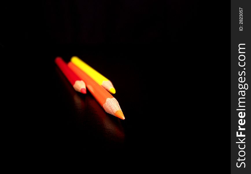 An orange colored pencil flanked by red and yellow colored pencils on each side on a black background. An orange colored pencil flanked by red and yellow colored pencils on each side on a black background.
