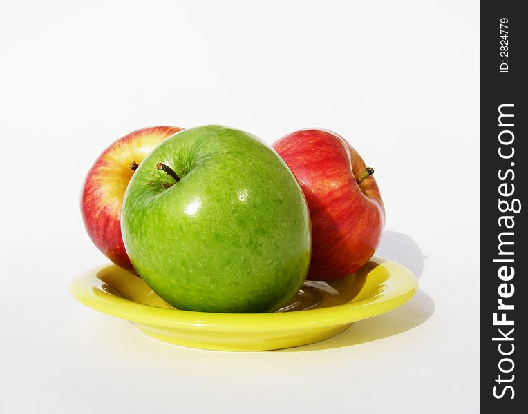 One green and two red apples lay on a yellow plate. One green and two red apples lay on a yellow plate.